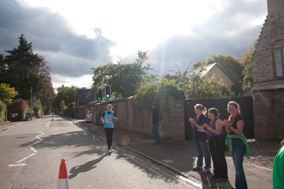 Girl running on road on the left, people clapping on right.